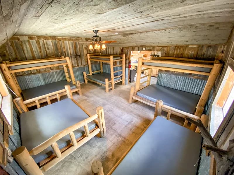 A rustic bunkhouse sleeping room with log-framed bunk beds arranged around an open center aisle.